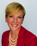 Portrait of Gretchen Wood smiling with short blonde hair, wearing a pink blazer and a 3 layer pearl necklace