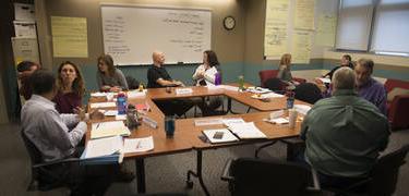 Second year faculty paired off in discussions around a square table.